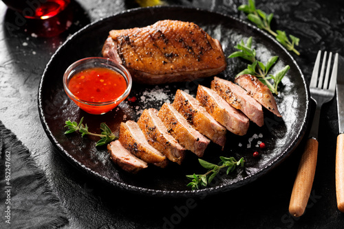 Roasted duck breast served with sauce and fresh herbs. Black background. photo