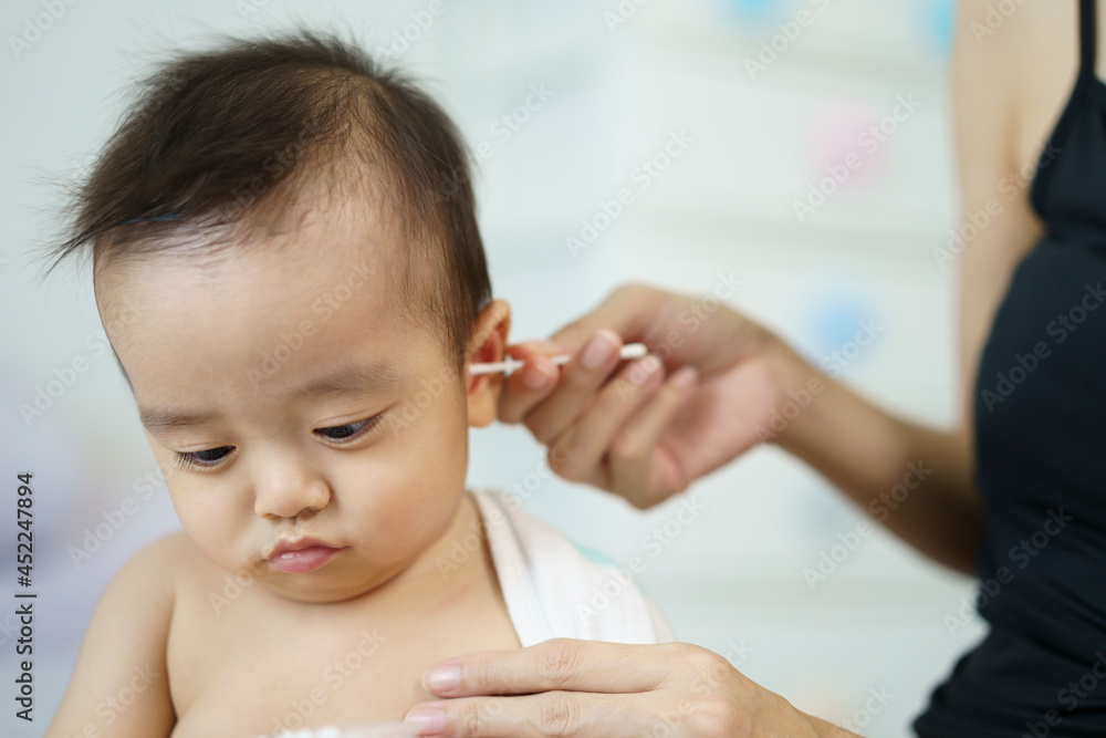 Asian mother is cleaning ear to her baby boy with cotton swab after a bath in bedroom. Asian mother is cleaning ear to her baby boy with cotton swab after a bath in bedroom.