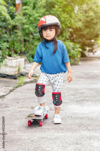 Portrait image of 3-4 years old childhood. A little Asian child girl play and riding a skateboard. She wearing safety helmet. At the park. Sport and exercise. Hobby