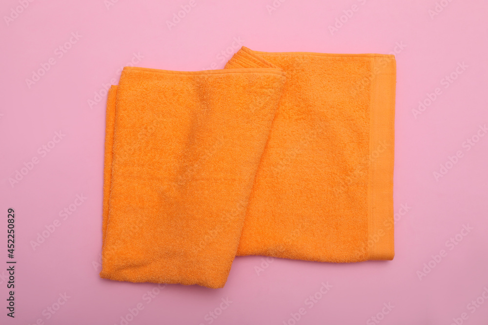 Folded orange beach towel on pink background, top view Folded orange beach towel on pink background, top view