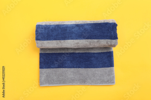 Rolled striped beach towel on yellow background, top view