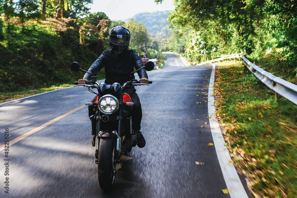 Obraz premium Man in a black helmet rides classic motorcycle on the road among autumn forest. Lifestyle or hobby of grown up man