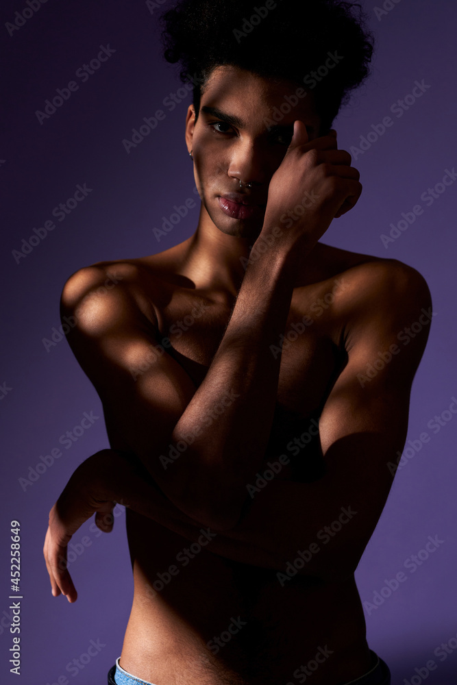 Portrait of young shirtless athletic man in shadow. Transgender model standing in casual pose Portrait of young shirtless athletic man in shadow. Transgender model standing in casual pose