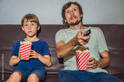 Father and son watching TV and eat popcort in evening at home