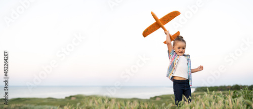 Healthy active child girl plays alone with a toy airplane on a summer field launches into the sky and dreams of becoming a pilot or stewardess. Spoils kid sky background Banner.