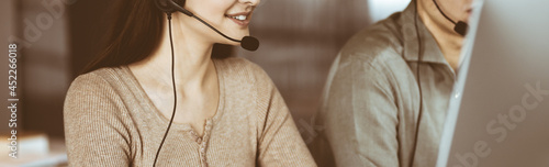 Two young people in headsets are talking to the clients, while sitting at the desk in an office. Focus on woman. Call center operators at work photo