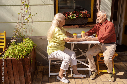 Positive senior pair of sweethearts at small table in street cafe