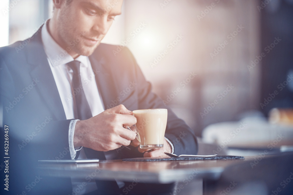 Confident young man in full suit enjoying coffee while sitting in the restaurant Confident young man in full suit enjoying coffee while sitting in the restaurant