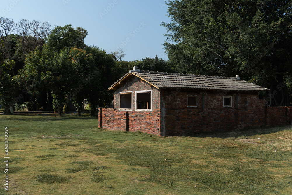 The old brick building set up on the grass. It is near by a lot of tree.