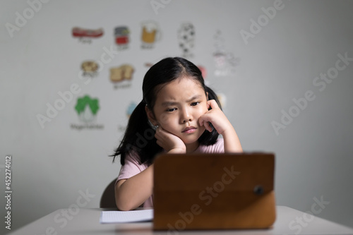 asian child student or kid girl stressed thinking and unhappy learning on computer tablet video call or frown bored to study only by smartphone or people learn from home school by english vocabulary