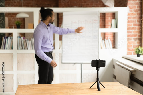 Wallpaper Mural African young male teacher blogger record webinar educational class use cell phone on tripod, explain written information pointing on flip chart. Improve language skills, tutoring, education concept Torontodigital.ca