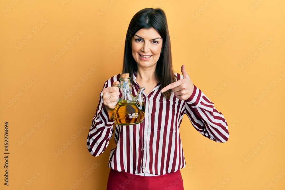 Young hispanic woman holding olive oil can smiling happy pointing with hand and finger Young hispanic woman holding olive oil can smiling happy pointing with hand and finger