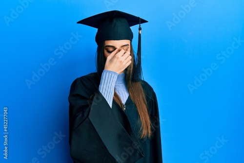 Beautiful brunette young woman wearing graduation cap and ceremony robe tired rubbing nose and eyes feeling fatigue and headache. stress and frustration concept.