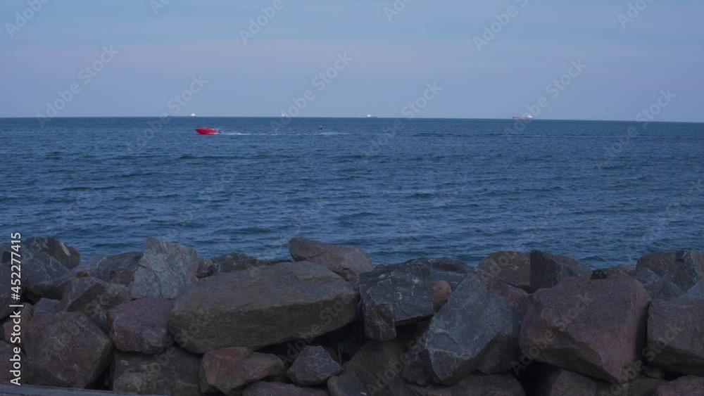 Beautiful seascape. A man in the background is tow-in surfing behind red boat. Rest at the seaside resort. Beautiful blue sea waves and the horizon with ships. Extreme water sports Beautiful seascape. A man in the background is tow-in surfing behind red boat. Rest at the seaside resort. Beautiful blue sea waves and the horizon with ships. Extreme water sports