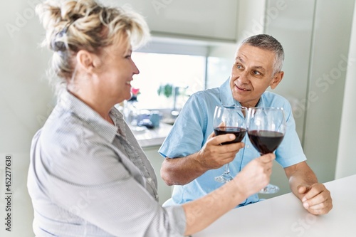 Senior caucasian couple smiling happy toasting with wine at the kitchen.