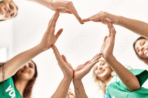 Group of young volunteers woman smiling happy make heart symbol with hands together at charity center. photo