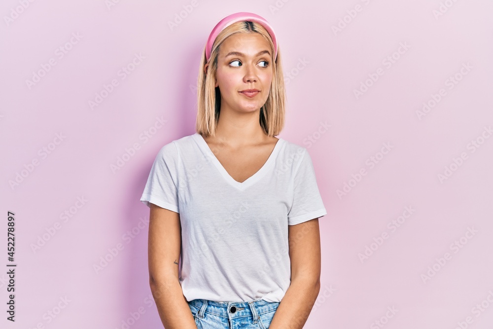 Beautiful blonde woman wearing casual white t shirt smiling looking to the side and staring away thinking. Beautiful blonde woman wearing casual white t shirt smiling looking to the side and staring away thinking.