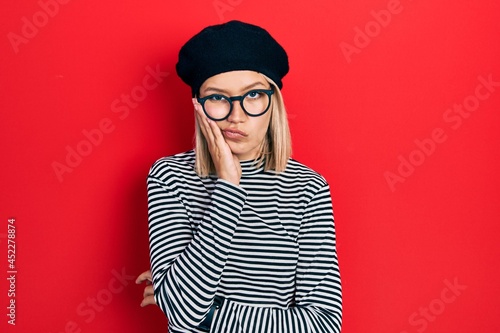 Beautiful blonde woman wearing french look with beret an glasses thinking looking tired and bored with depression problems with crossed arms.