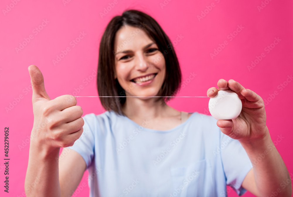 Beautiful young woman use dental floss on pink background Beautiful young woman use dental floss on pink background