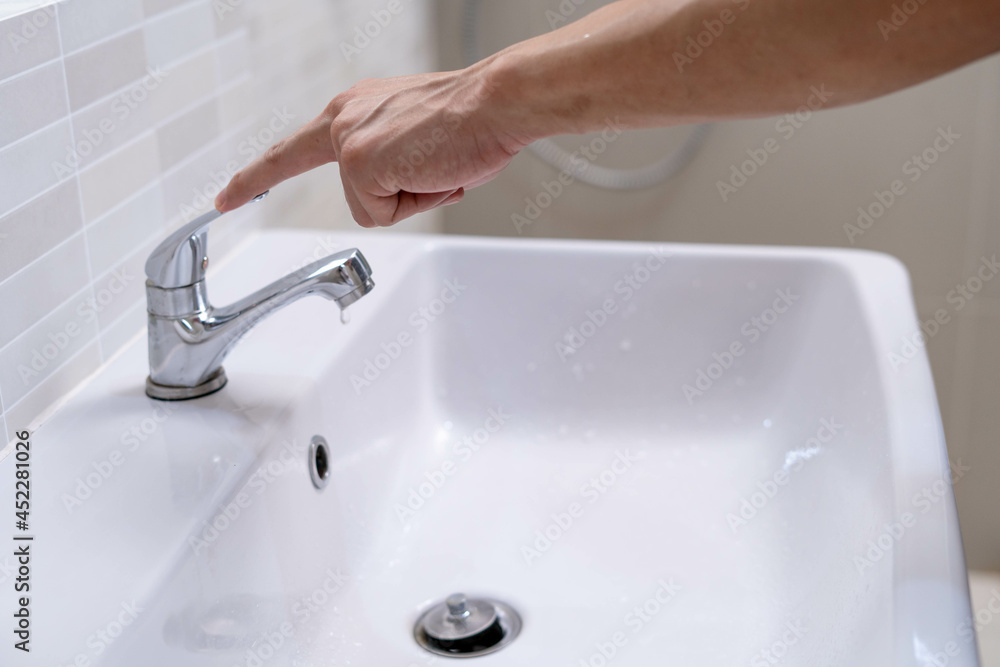 The faucet in the bathroom with running water. Man keeps turning off