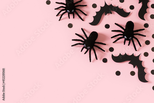 Halloween card with black spiders, bat and confetti on pink background © Denira