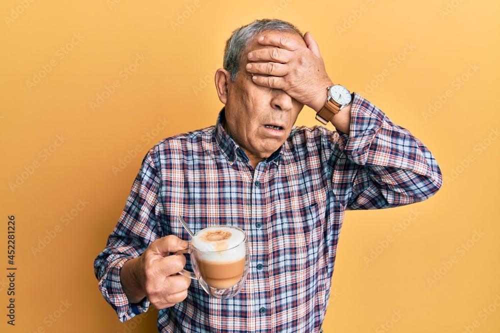 Handsome senior man with grey hair drinking a cup coffee covering eyes with hand, looking serious and sad. sightless, hiding and rejection concept Handsome senior man with grey hair drinking a cup coffee covering eyes with hand, looking serious and sad. sightless, hiding and rejection concept