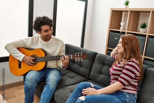 Young couple smiling happy playing classical guitar sitting on the sofa at home.