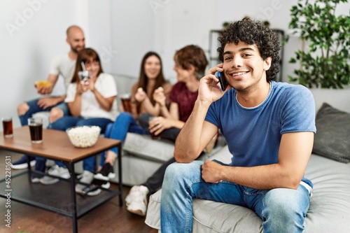 Group of young friends having party sitting on the sofa at home. Man smiling happy talking on the smartphone at home.