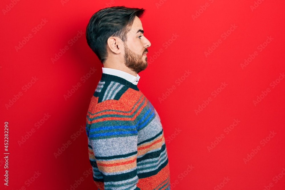 Handsome caucasian man with beard wearing elegant wool winter sweater looking to side, relax profile pose with natural face with confident smile.