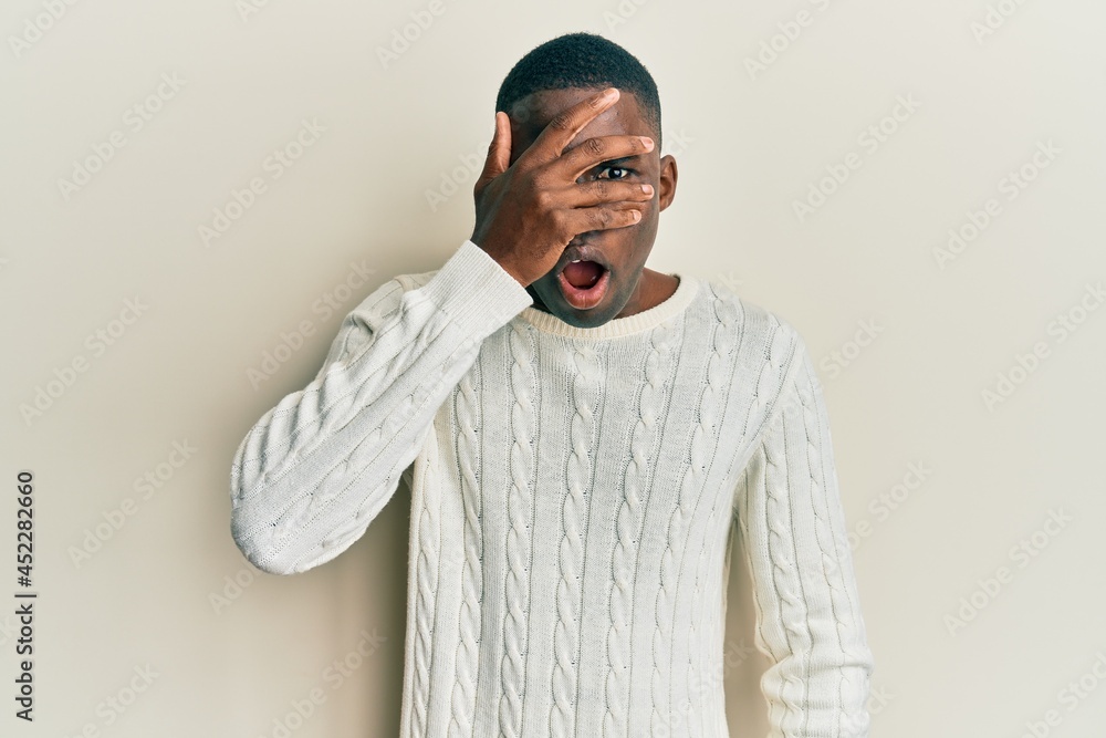 Young african american man wearing casual clothes peeking in shock covering face and eyes with hand, looking through fingers with embarrassed expression. Young african american man wearing casual clothes peeking in shock covering face and eyes with hand, looking through fingers with embarrassed expression.
