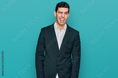 Handsome hispanic man wearing business clothes winking looking at the camera with sexy expression, cheerful and happy face.