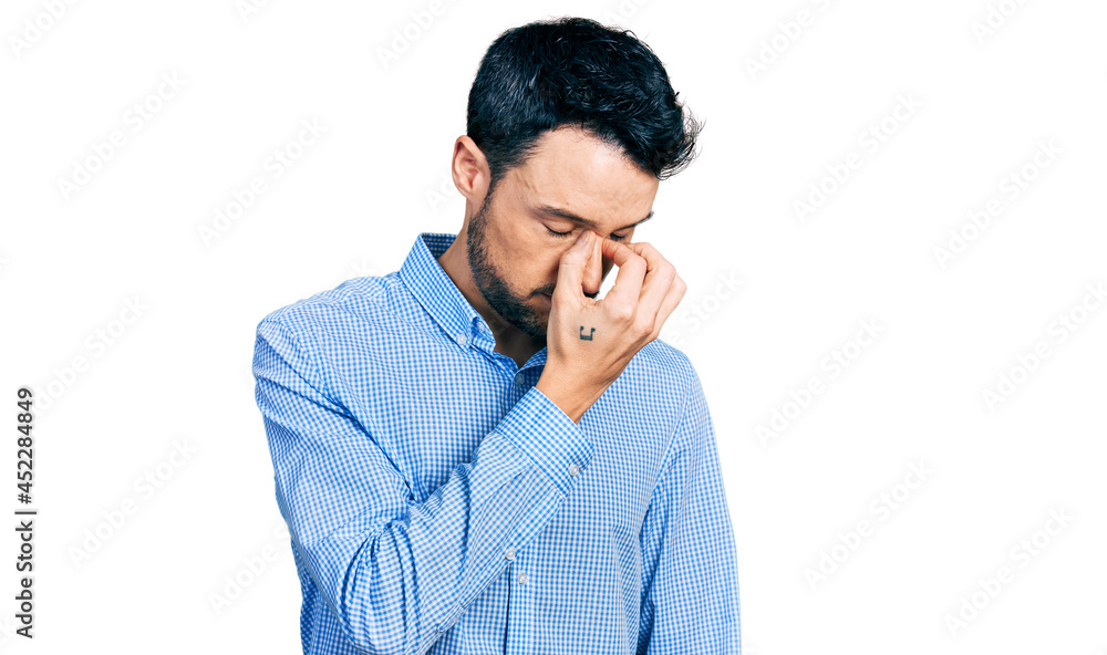Hispanic man with beard wearing casual business shirt tired rubbing nose and eyes feeling fatigue and headache. stress and frustration concept. Hispanic man with beard wearing casual business shirt tired rubbing nose and eyes feeling fatigue and headache. stress and frustration concept.