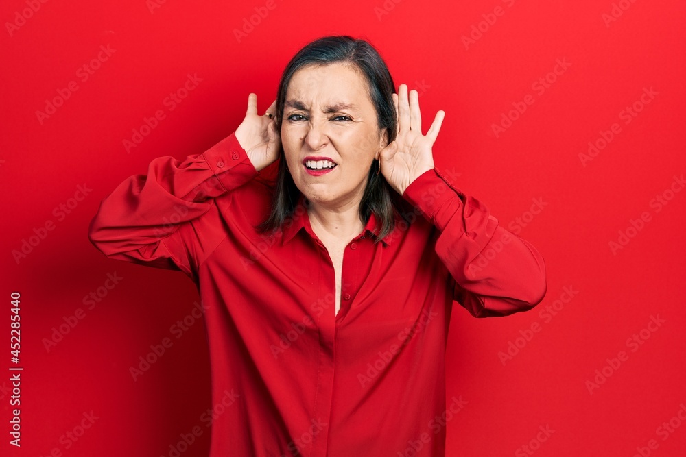 Middle age hispanic woman wearing casual clothes trying to hear both hands on ear gesture, curious for gossip. hearing problem, deaf Middle age hispanic woman wearing casual clothes trying to hear both hands on ear gesture, curious for gossip. hearing problem, deaf