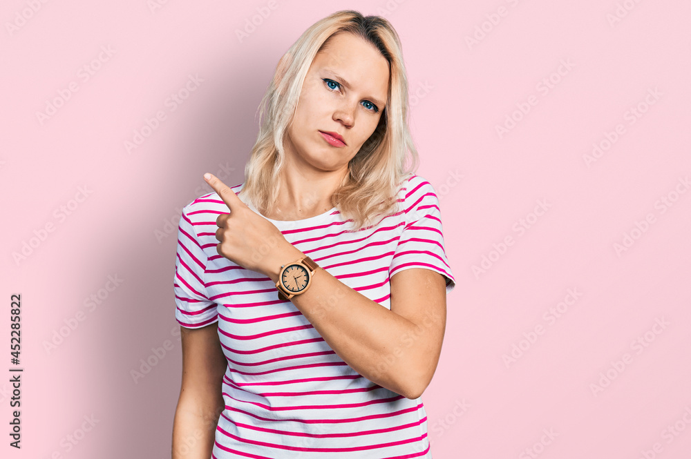 Young caucasian woman wearing casual clothes pointing with hand finger to the side showing advertisement, serious and calm face Young caucasian woman wearing casual clothes pointing with hand finger to the side showing advertisement, serious and calm face