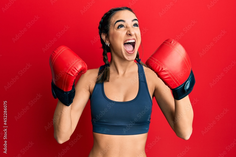 Young brunette girl using boxing gloves wearing braids angry and mad screaming frustrated and furious, shouting with anger looking up.