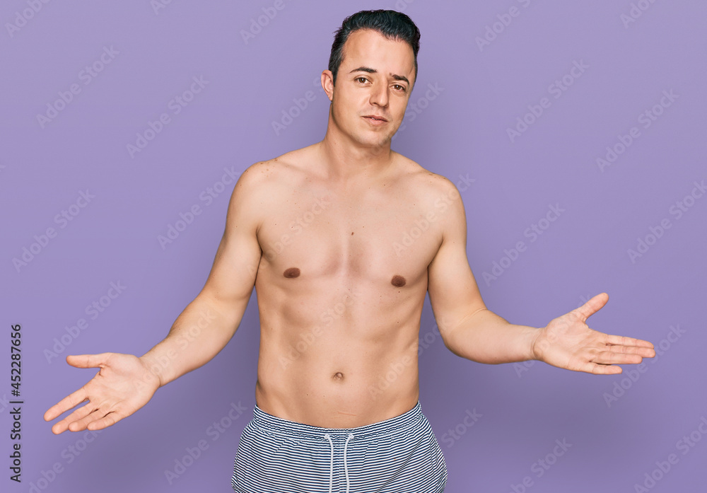 Handsome young man wearing swimwear shirtless clueless and confused with open arms, no idea concept. Handsome young man wearing swimwear shirtless clueless and confused with open arms, no idea concept.