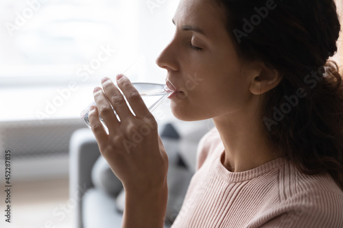 Woman hold glass makes sip of still water  close up side view face. Young female looking sick feels unwell reduces thirst drinks fresh aqua  keep diet  weight loss  healthcare  natural balance concept