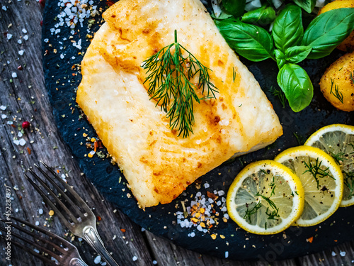 Canvas Print Fish dish - fried cod fillet with potatoes and vegetable salad served on stone p