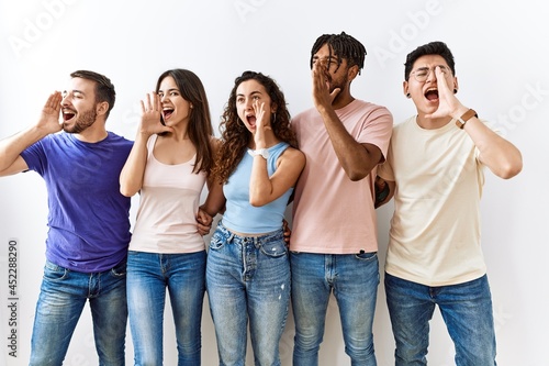 Group of young people standing together over isolated background shouting and screaming loud to side with hand on mouth. communication concept.