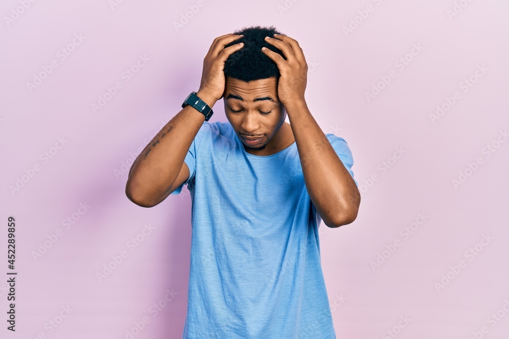 Young african american man wearing casual blue t shirt suffering from headache desperate and stressed because pain and migraine. hands on head. Young african american man wearing casual blue t shirt suffering from headache desperate and stressed because pain and migraine. hands on head.