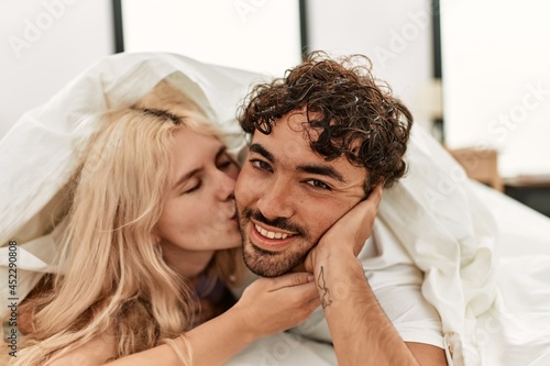 Young beautiful couple smiling happy covering with sheet lying on the bed.