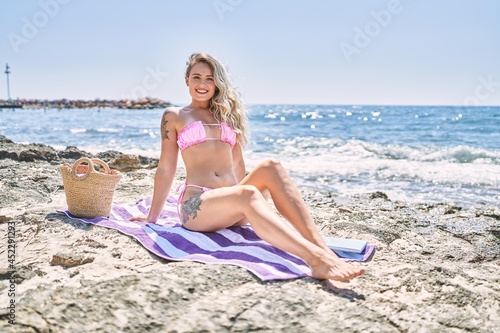 Young blonde girl wearing bikini sitting on the towel at the beach.