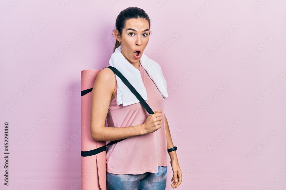 Young brunette woman holding yoga mat scared and amazed with open mouth for surprise, disbelief face Young brunette woman holding yoga mat scared and amazed with open mouth for surprise, disbelief face