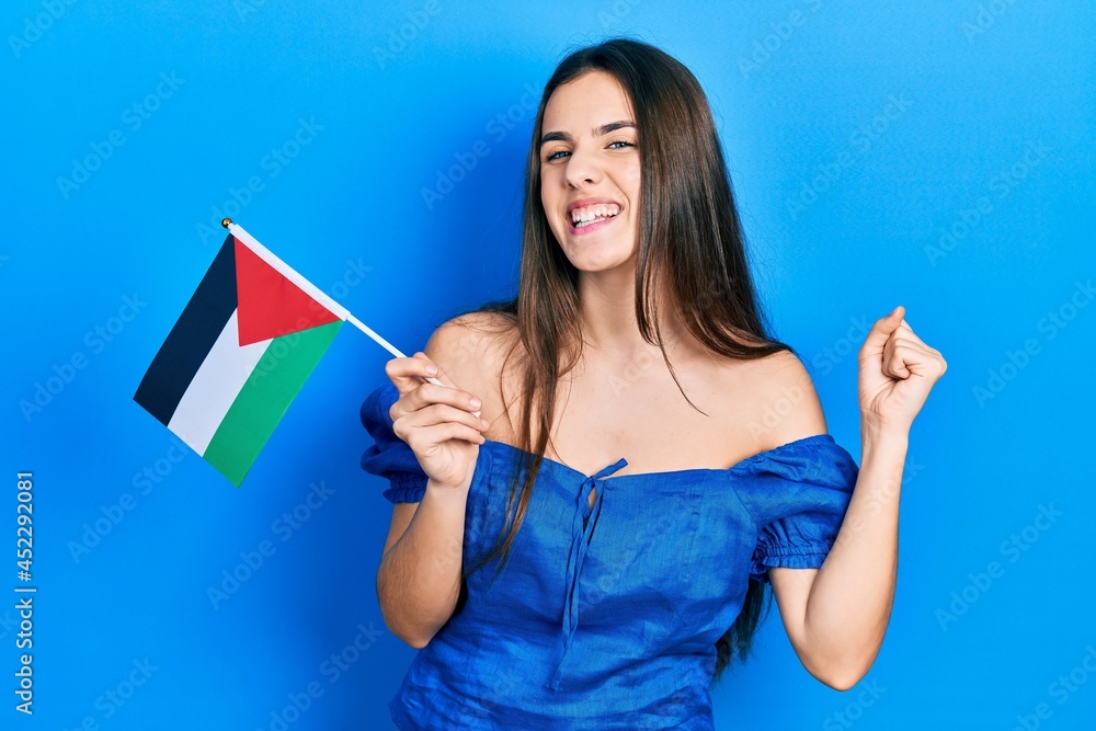 Young brunette teenager holding palestine flag screaming proud, celebrating victory and success very excited with raised arm Young brunette teenager holding palestine flag screaming proud, celebrating victory and success very excited with raised arm