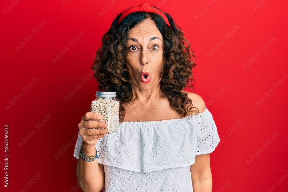 Middle age hispanic woman holding jar of beans scared and amazed with open mouth for surprise, disbelief face Middle age hispanic woman holding jar of beans scared and amazed with open mouth for surprise, disbelief face