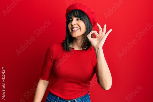 Young hispanic woman wearing french look with beret smiling positive doing ok sign with hand and fingers. successful expression. © Krakenimages.com