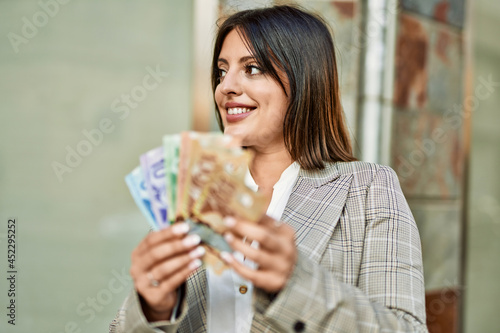 Young hispanic businesswoman smiling happy holding canadian dollars at the city.