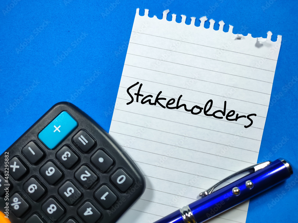 Business concept.Text Stakeholders writing on notepaper with pen and calculator on blue background. Business concept.Text Stakeholders writing on notepaper with pen and calculator on blue background.