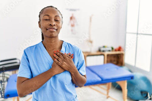 Black woman with braids working at pain recovery clinic smiling with hands on chest with closed eyes and grateful gesture on face. health concept.