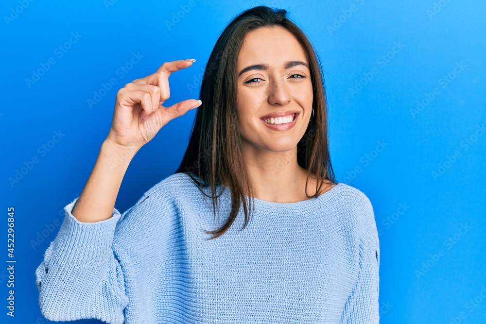 Young hispanic girl wearing casual clothes smiling and confident gesturing with hand doing small size sign with fingers looking and the camera. measure concept. Young hispanic girl wearing casual clothes smiling and confident gesturing with hand doing small size sign with fingers looking and the camera. measure concept.